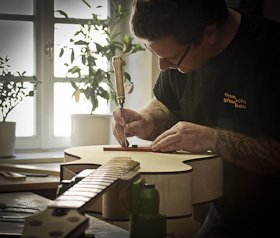 Portrait des Gitarrenbaumeisters Thomas Ochs in seiner Werkstatt in Kemmern. Einpassen der Saitenreiter am Steg eines Akustik-Basses mit True Temperament Griffbrett.
