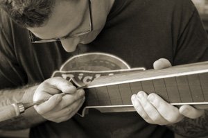 Portrait des Gitarrenbaumeisters Thomas Ochs in seiner Werkstatt in Kemmern. Abstechen von Leim am Binding eines E-Gitarren Griffbretts